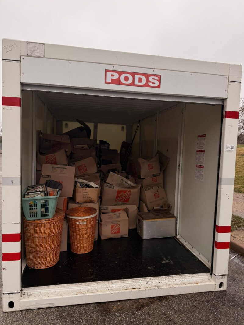 An open PODS moving container is packed tightly with cardboard Home Depot boxes, wicker hampers, and a laundry basket.
